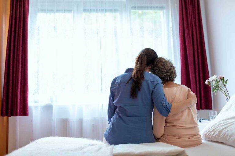 An older adult participating in a gentle group activity with supportive caregivers and peers in a well-lit community room.